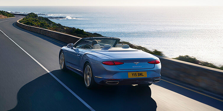 Bentley Budapest New Bentley Continental GTC Azure convertible rear view in Light Windsor blue paint with 22 inch ten spoke wheels driving dynamically on an ocean road in the sunshine